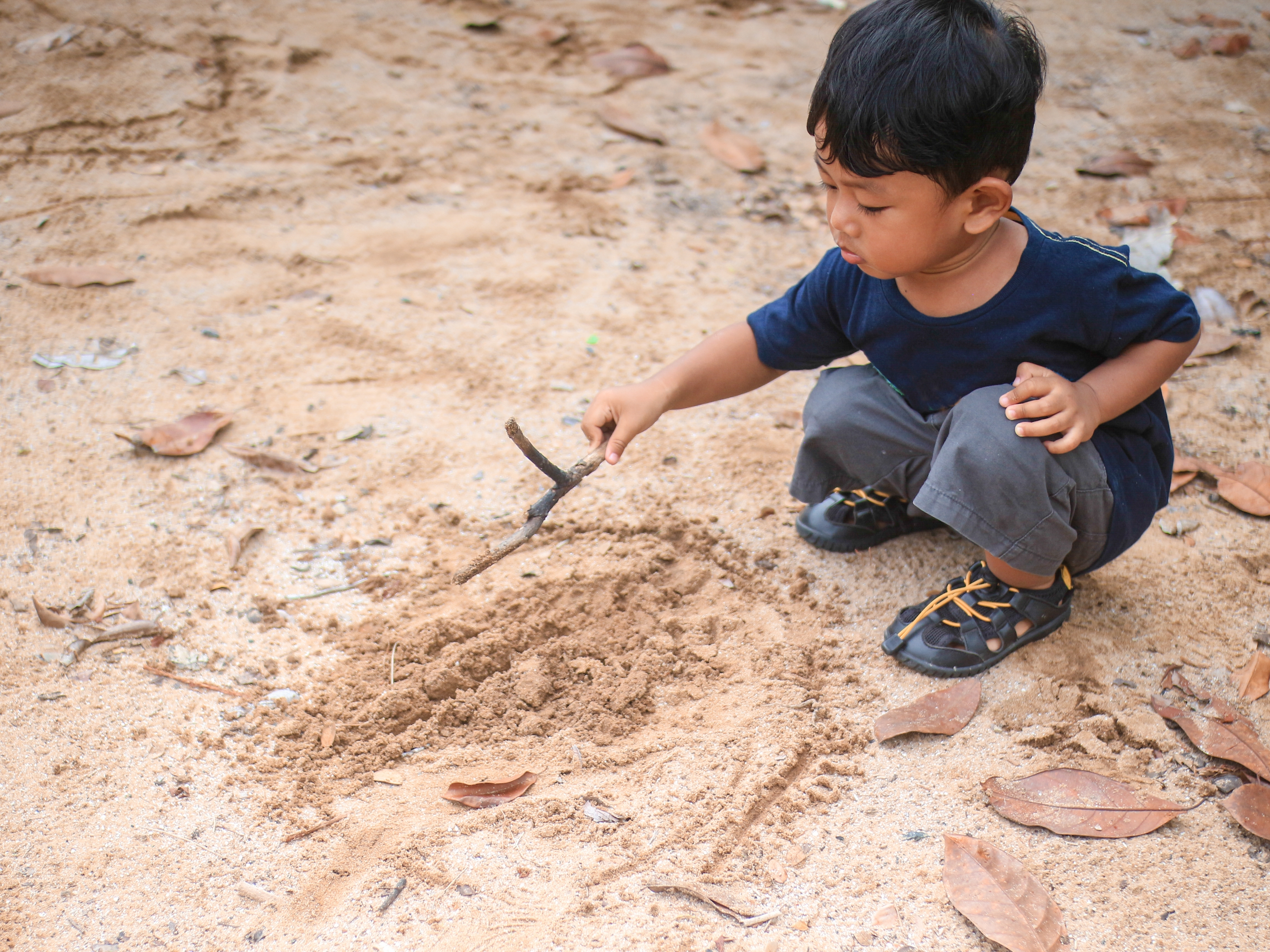 preschooler drawing with stick in sand
